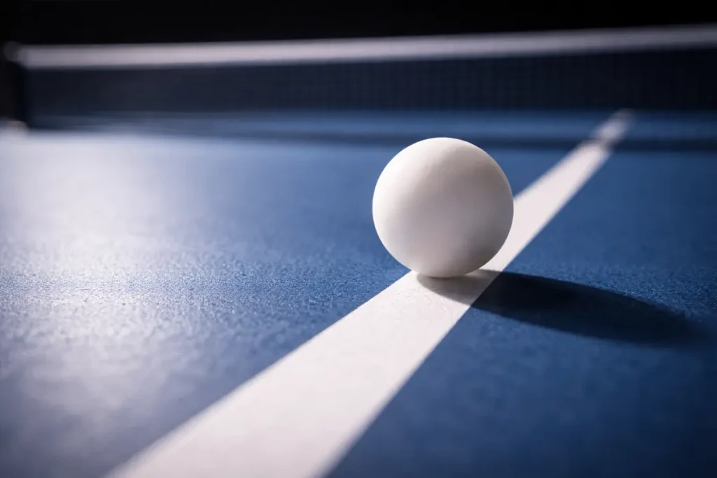 Pelota de tenis de mesa sobre la línea blanca de una mesa azul de competición